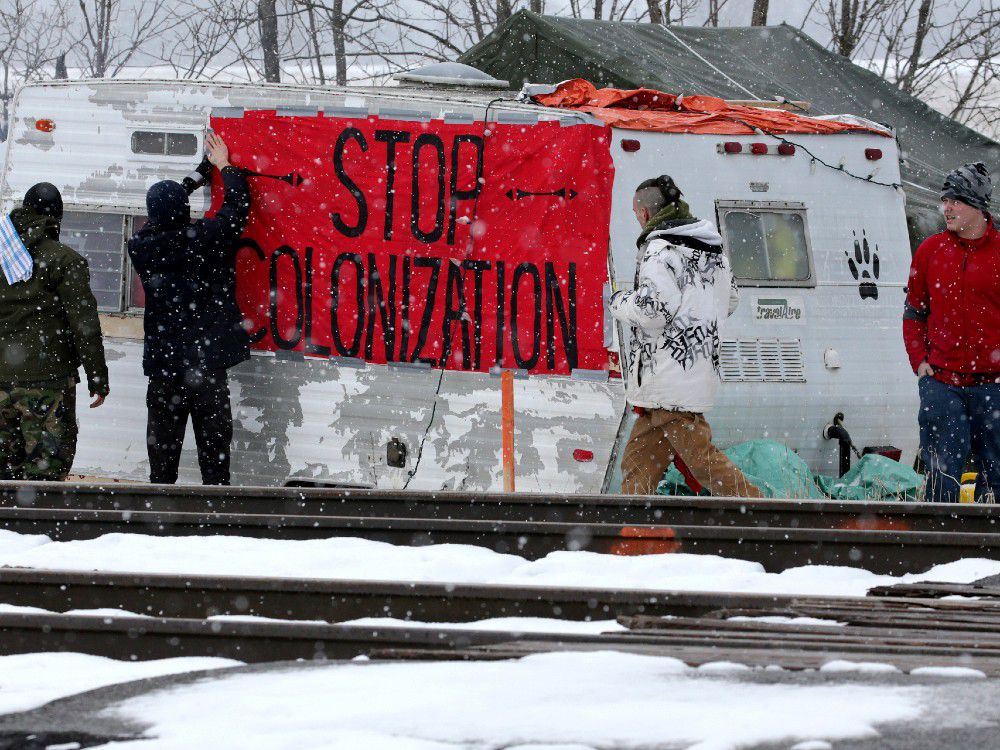  First Nations members of the Tyendinaga Mohawk Territory place a sign reading “Stop Colonization” to a camper at a blockade of train tracks servicing Via Rail, as part of a protest against British Columbia’s Coastal GasLink pipeline, in Tyendinaga, Ontario, Canada February 13, 2020.