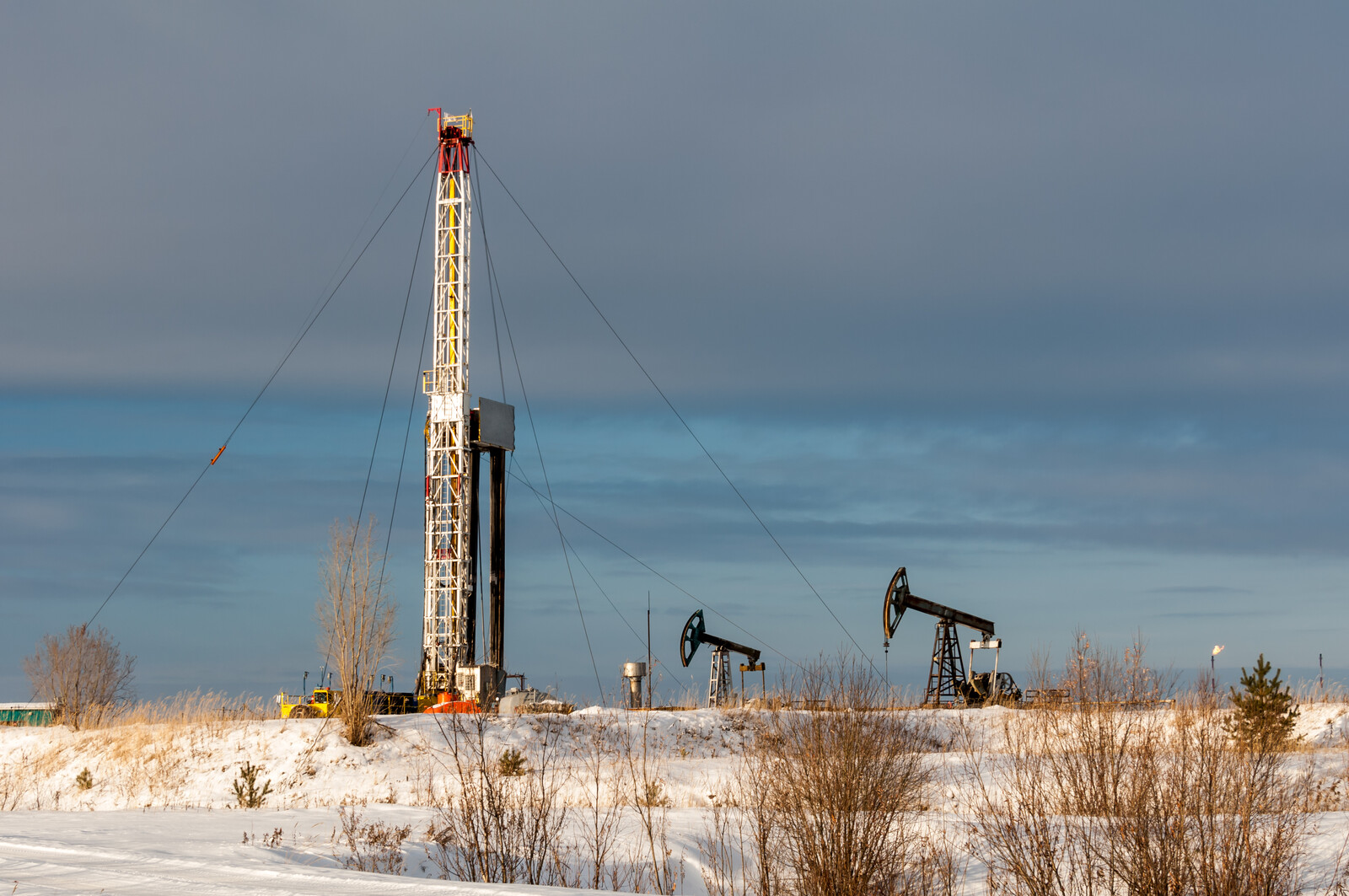 Drilling rig in winter with pump jacks in background.