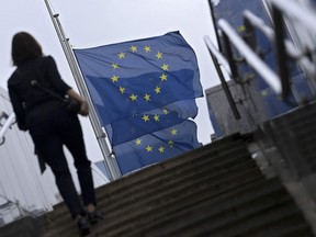 A woman climbs stairs next to European flags flying at half-mast during a meeting of EU energy ministers to find solutions to rising energy prices at the EU headquarters in Brussels on Septembre 9, 2022.