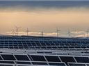 Solar panels at the Travers Solar Project with wind turbines behind them west of Lomond.